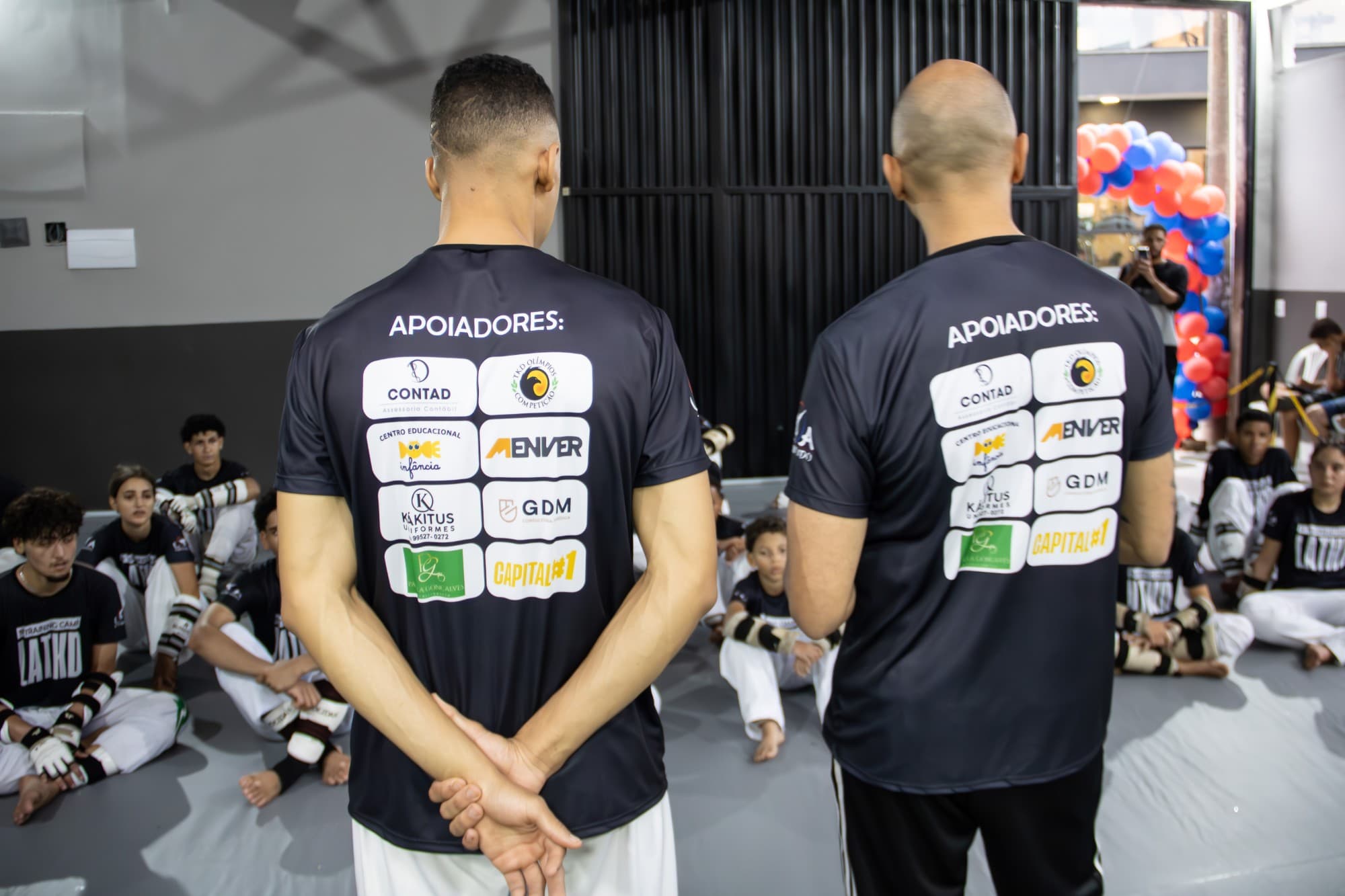 Atletas de costas mostrando o uniforme da equipe com os logos dos apoiadores impressos