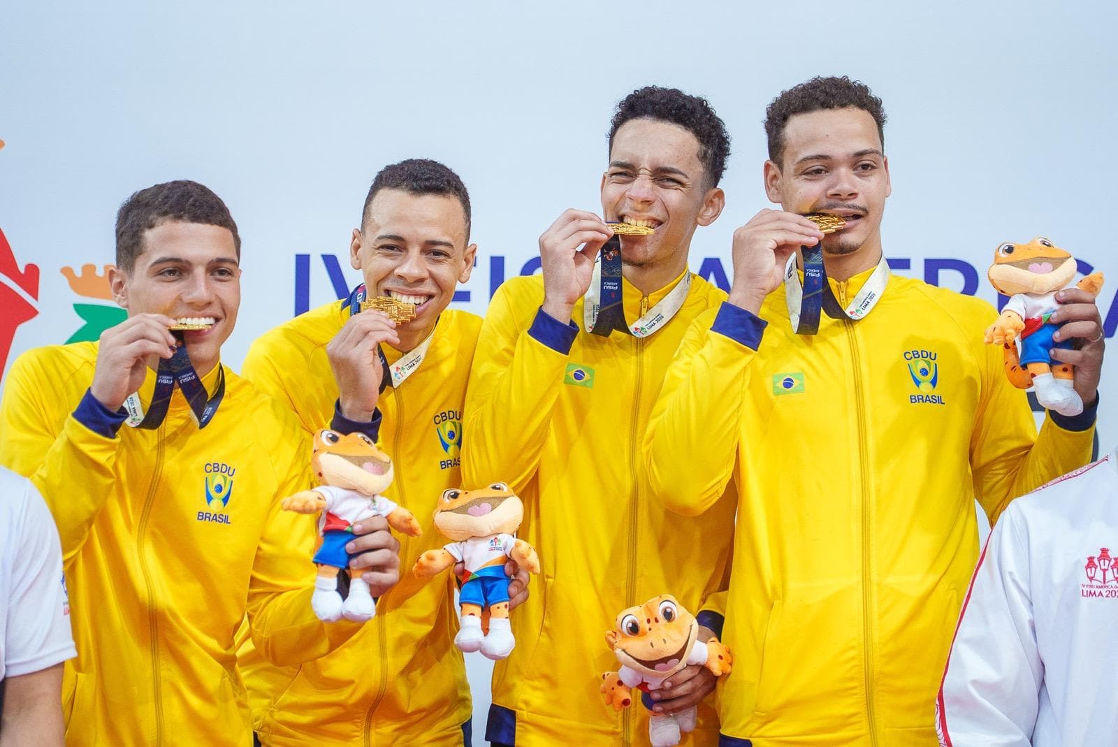Quatro atletas brasileiros no pódio, mordendo as medalhas de ouro